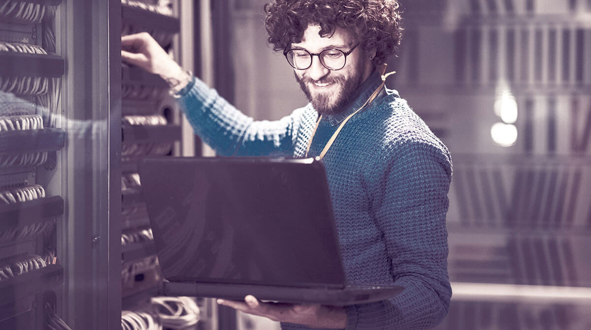 Mann mit Lapotop arbeitet lächelnd an Serverschrank