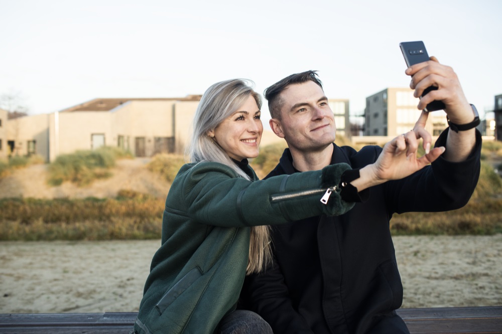 Mann und Frau stehen vor einem Haus und machen ein Selfie