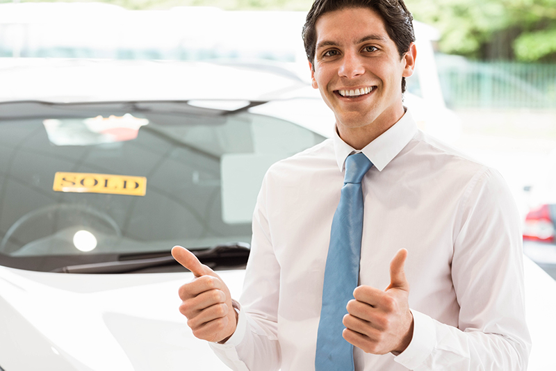 Ein Autoverkäufer lächelt zufrieden und zeigt seine Daumen hoch.