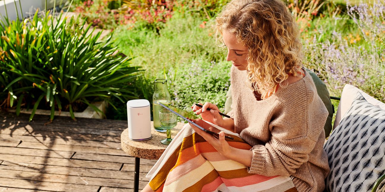 Telekom Speedbox ist auf einem Tisch platziert im Garten und Frau bedient ein Tablet
