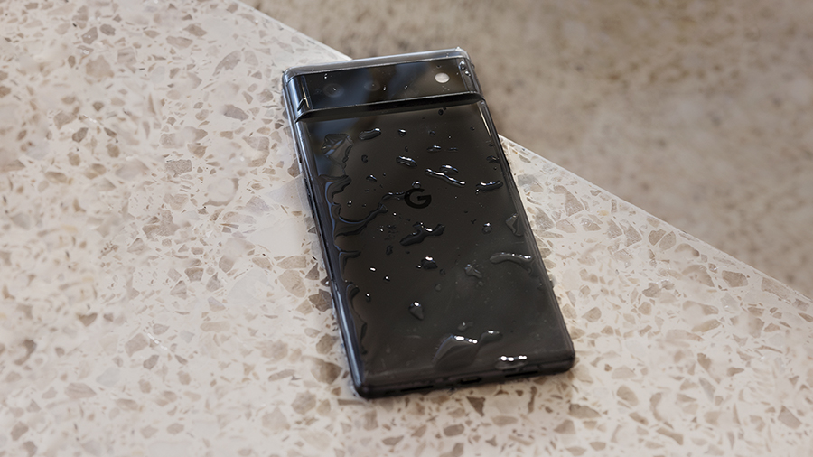 Ein nasses Google Pixel 6 Pro in der Farbe Stormy Black liegt mit der Frontansicht auf einer Steinbank. Das Display ist nass.
