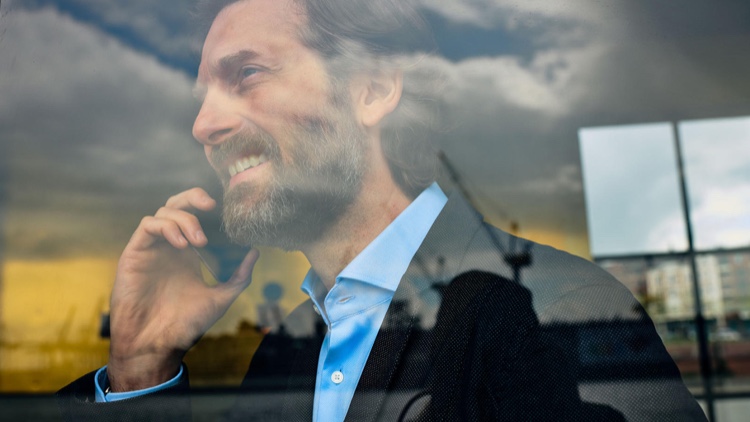 Smiling man in a suit looks out of window while talking on the phone