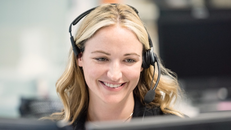 Lächelnde Frau mit Headset vor einem Monitor