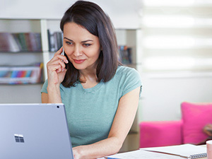 Eine Frau im mintfarbenen Dress sitzt arbeitet am Laptop und telefoniert.