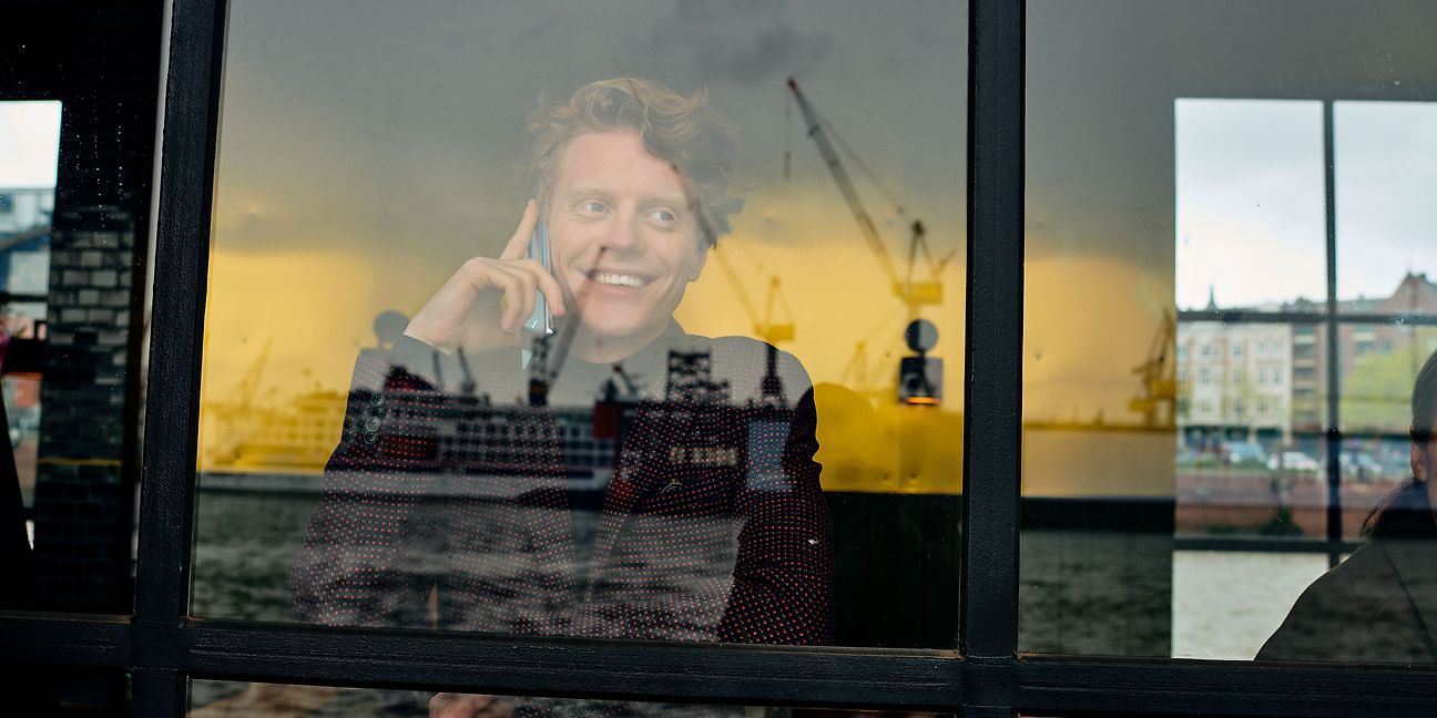 Mann guckt durch Fenster am Hafen mit Handy am Ohr