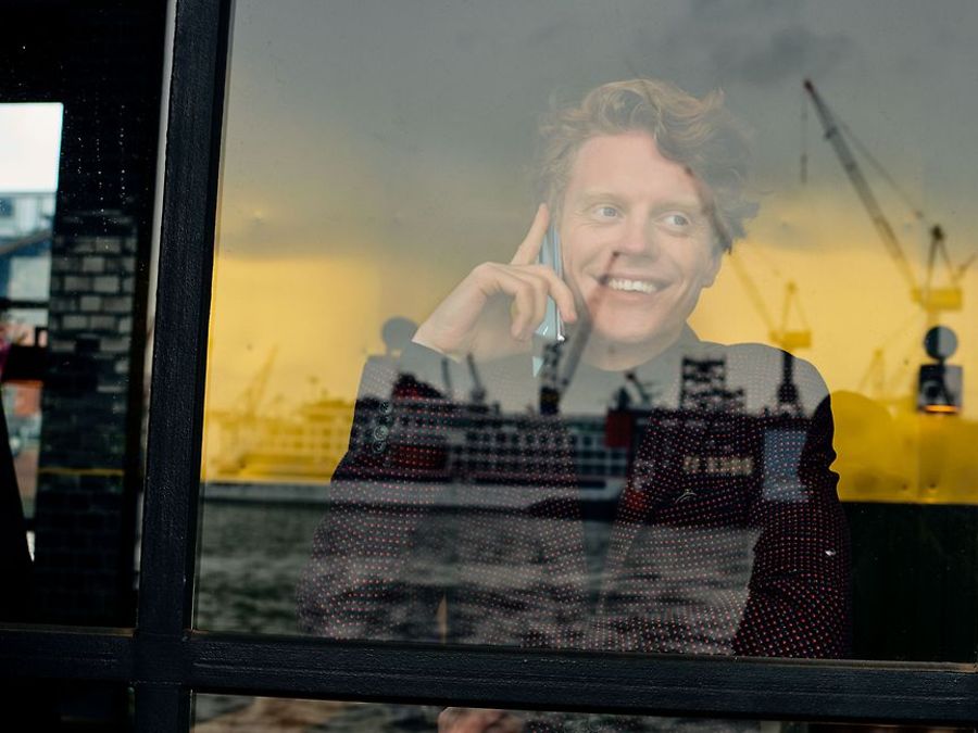 Mann guckt durch Fenster am Hafen mit Handy am Ohr