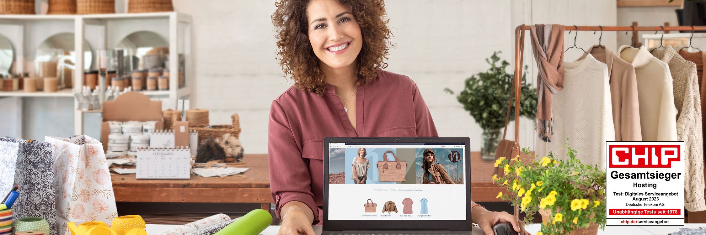 Fröhliche Geschäftsfrau präsentiert in ihrem Laden auf einem Laptop ihren neuen mit der Telekom erstellten Webshop.