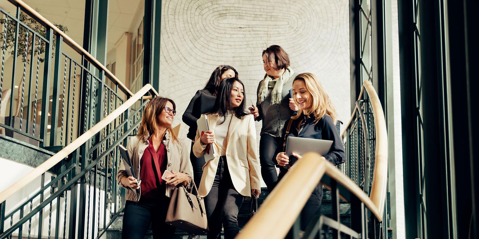 Fünf Frauen in Businesskleidung gehen Treppenstufen hinunter und unterhalten sich währenddessen.