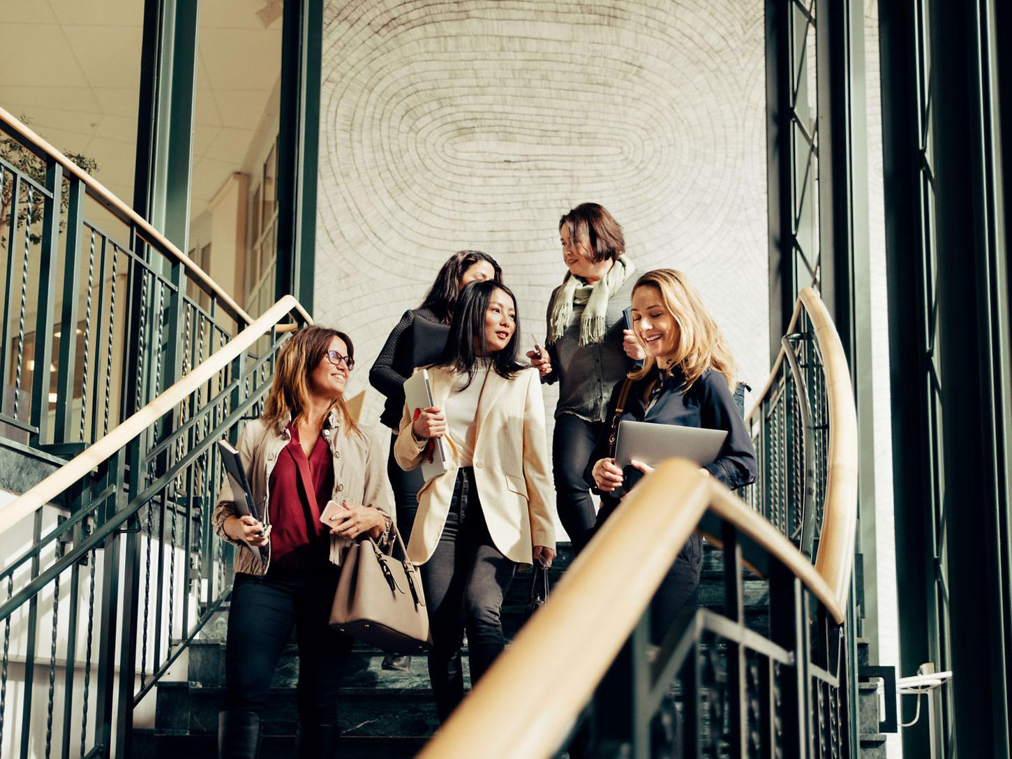 Fünf Frauen in Businesskleidung gehen Treppenstufen hinunter und unterhalten sich währenddessen.