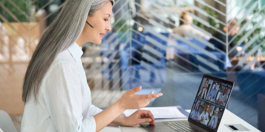 Frau mit Headset vor Laptop in Online-Meeting