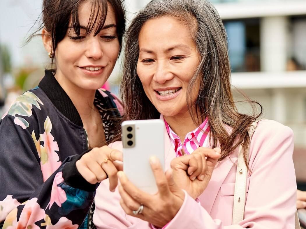 Zwei Frauen schauen gemeinsam auf ein weißes Smartphone