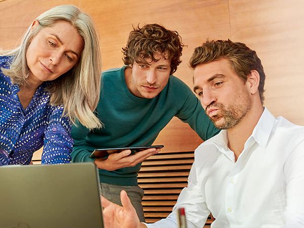 Eine Frau und zwei Männer schauen gemeinsam auf einen Laptop