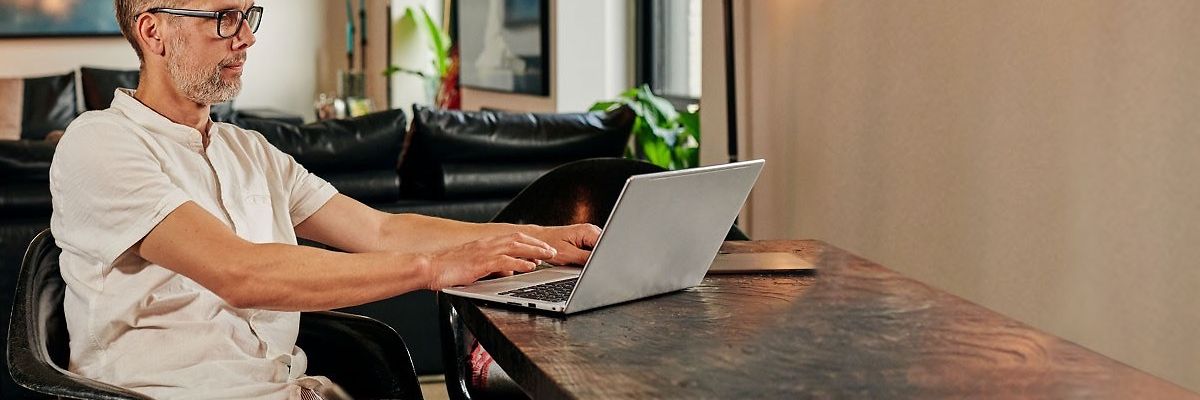 Mann sitzt im Wohnzimmer und arbeitet an seinem Laptop