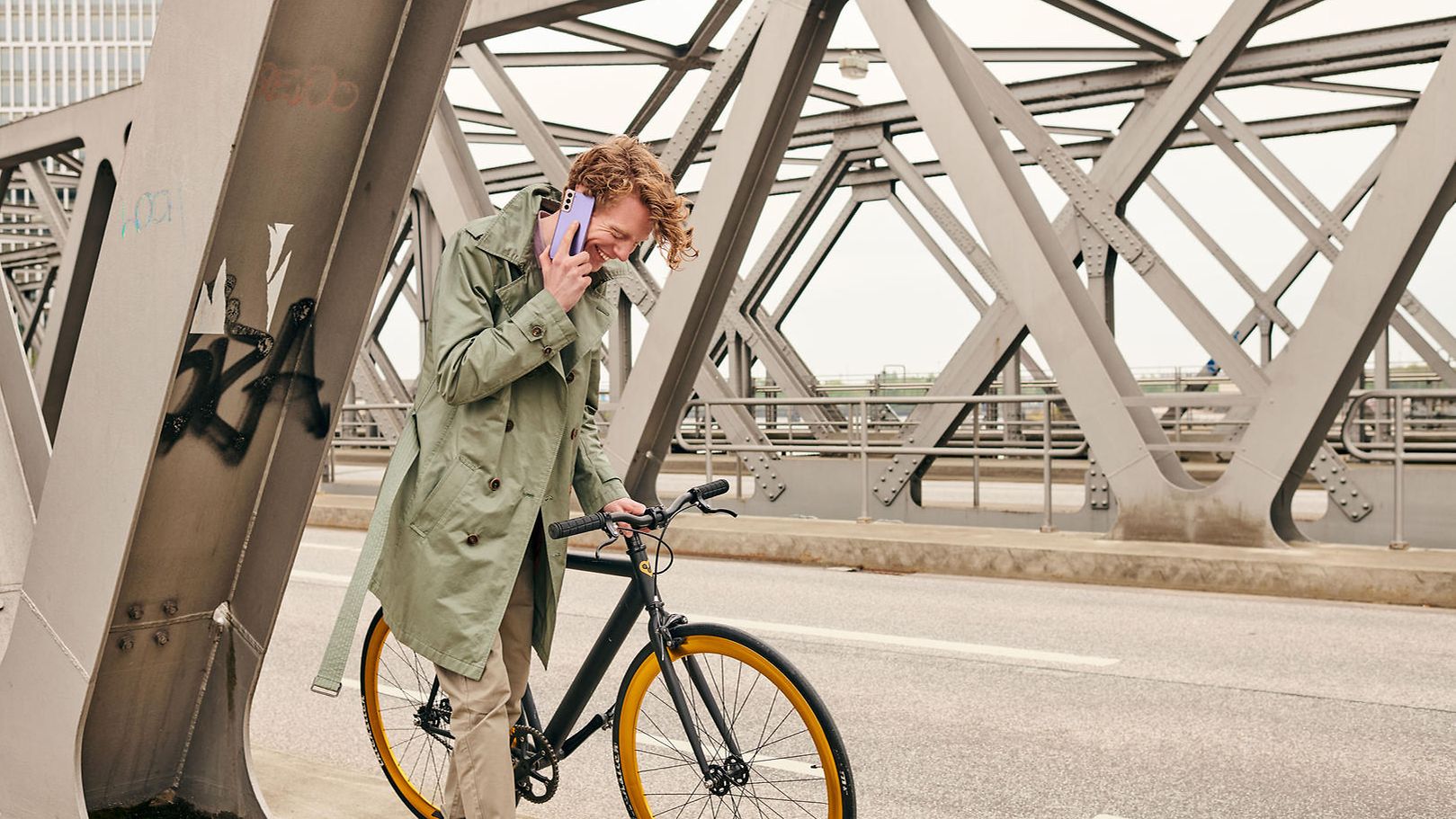 Mann schiebt Fahrrad über Brücke und telefoniert dabei.