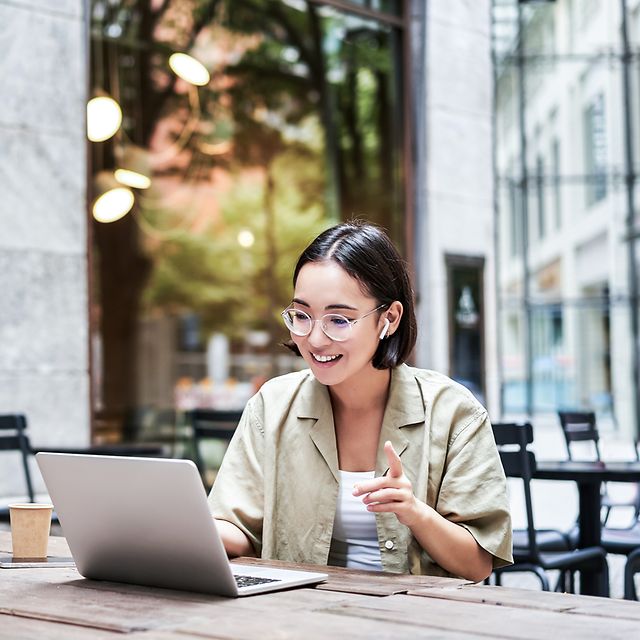 Eine Frau sitzt vor ihrem Laptop und telefoniert.
