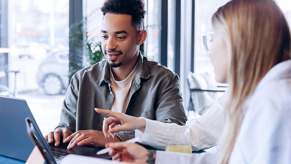 Eine Frau und ein Mann sitzen vor ihren Laptops und unterhalten sich.