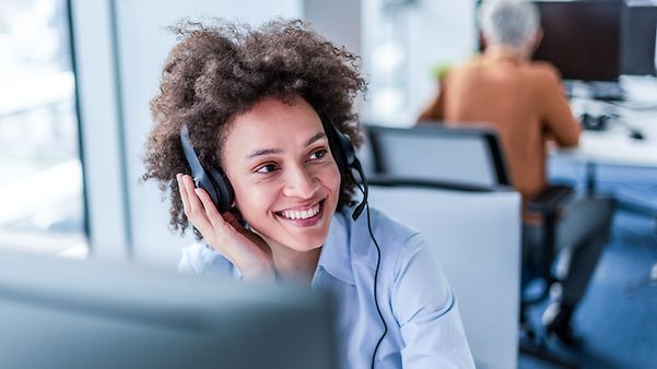 Frau mit wuscheligen Haaren sitzt lächelnd mit Headset in einem Büro und nutzt CompanyFlex Flat für Auslandsgespräche.