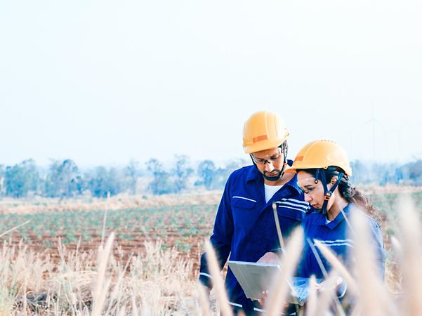 Zwei Personen stehen draußen in Arbeitskleidung und schauen auf ein Laptop.