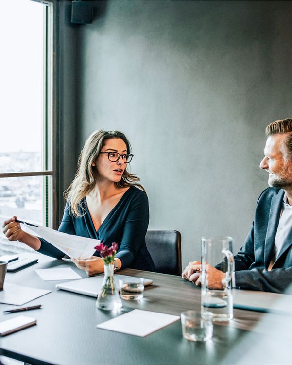 Eine seriös aussehende Businessrunde am Tisch sitzend mit Unterlagen auf dem Tisch und Wassergläsern