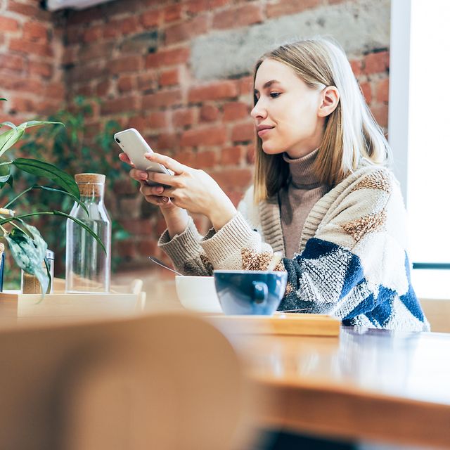 Young woman using Microsoft 365 on her smartphone while sitting at a table