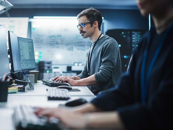 Portrait of a thoughtful engineer working on a desktop computer in a technological office environment.