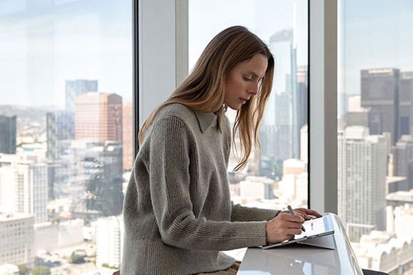 Woman sitting at her desk in front of a window, working with a Surface in her hand