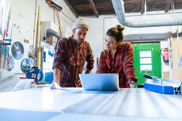 Two colleagues look at a laptop in a workshop