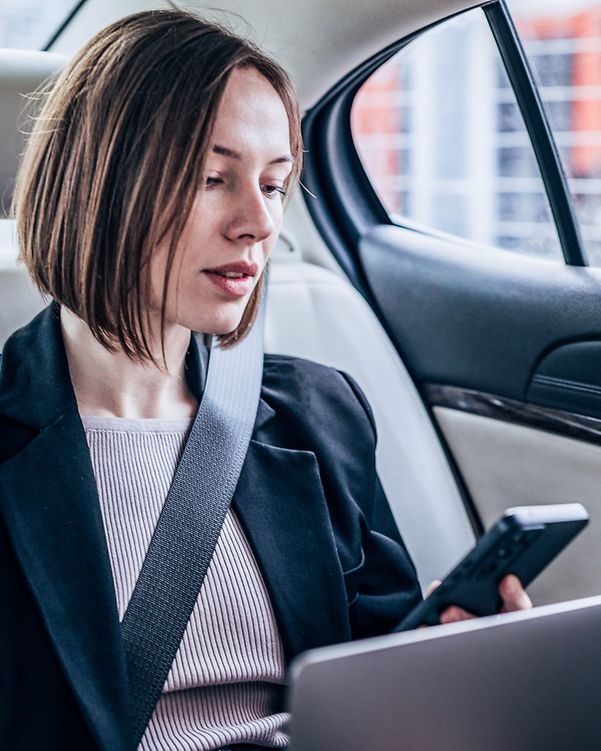 A businesswoman sits in her car and holds a Microsoft Teams conference.