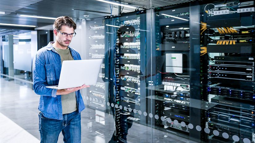 An employee is standing in the server room with a notebook.