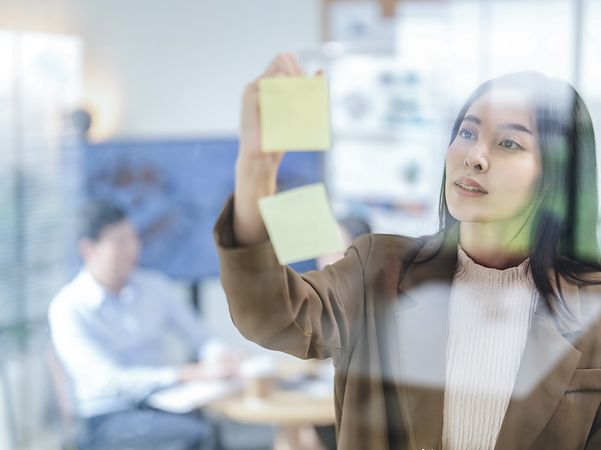 A woman sticks a Post-It note to a glass wall.