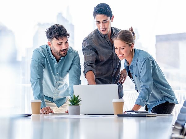 Three people are looking at a laptop screen and discussing a project.