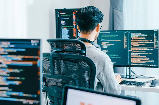 Man seen from behind at computers in front of several screens