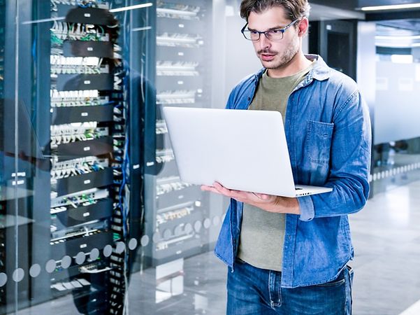 A man is standing in the server room looking at a computer screen.