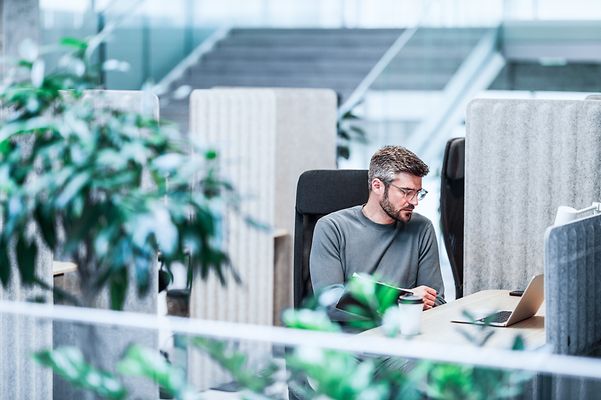 A colleague sits in the office and looks at his notebook with Zoom X Rooms.