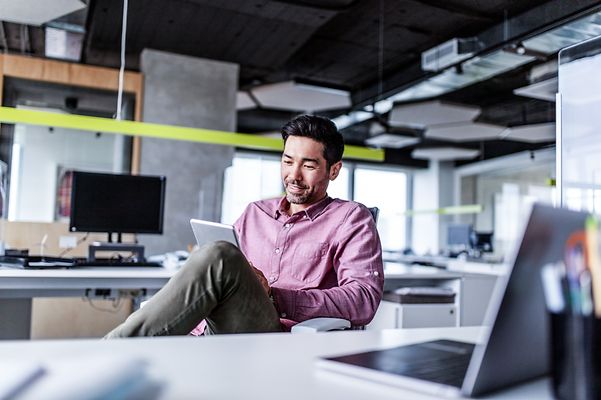 A Japanese colleague sits in the office and smiles as he looks at his notebook, which is running Zoom X Rooms.