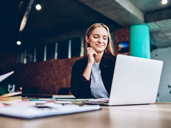 Young woman has successfully used DocuSign and is sitting smiling in front of her laptop.