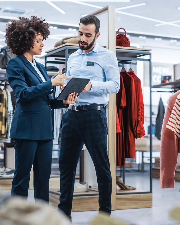 A woman and a man are standing in a clothing shop, approving a business transaction on a tablet using DocuSign.