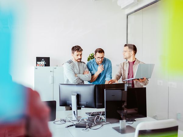 Three men are standing in front of a desk discussing suitable telephone systems.