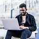 A young man types on his laptop and smiles.