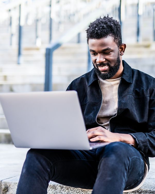 A young man types on his laptop and smiles.