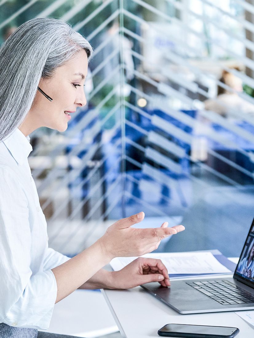 A woman talks on the phone in front of her laptop via a headset and provides information about Microsoft Dynamics 365.
