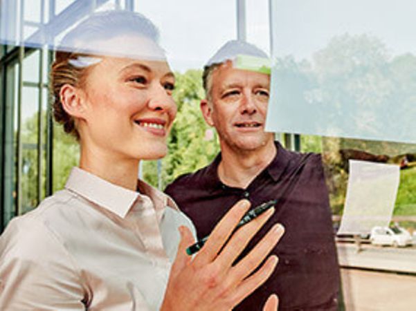 A woman and a man smile as they look together at a whiteboard.