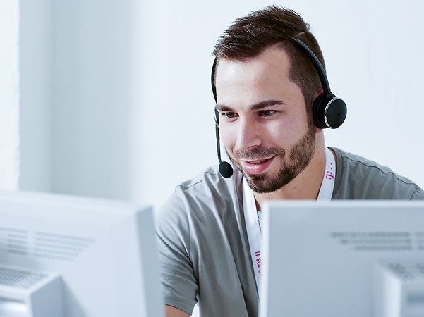 A man sits smiling with a headset in front of two monitors.
