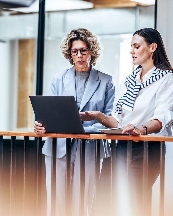 Two businesswomen are chatting whilst using a laptop.