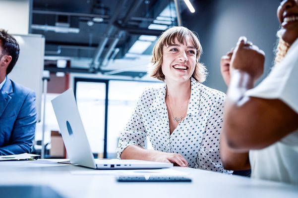 Colleagues in business attire smile during a discussion at a meeting in the office.