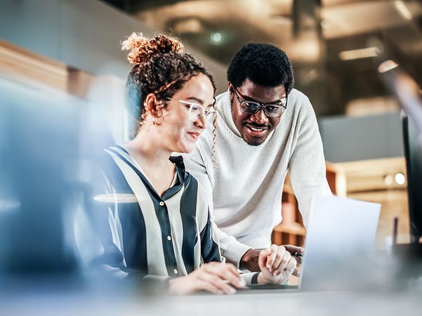 Porträt von zwei Kollegen, die einen Laptop benutzen, um über die CRM-Beratung der Telekom zu sprechen