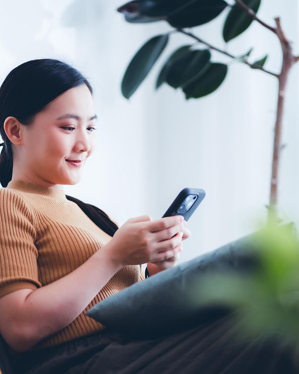 Woman sitting happily on the sofa, smiling and using her smartphone