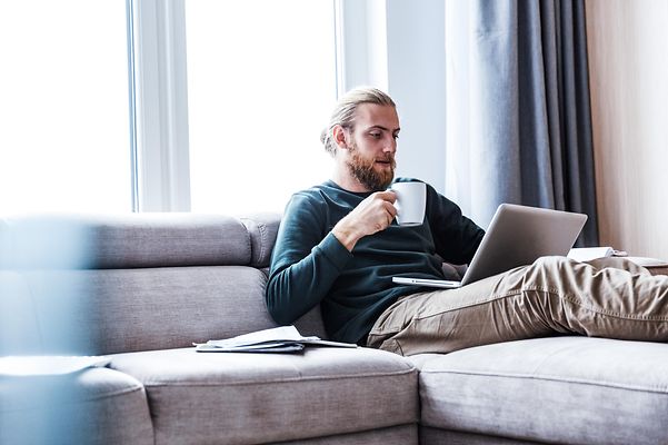 Concentrated young bearded man sitting at home using a laptop.