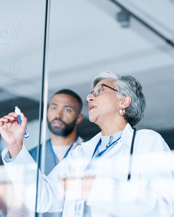 Several doctors stand in front of a planning board in a hospital, which is connected via 5G campus networks.