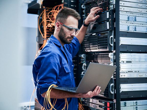 A technician works on a server cabinet with a laptop and takes care of providing broadband capacity.